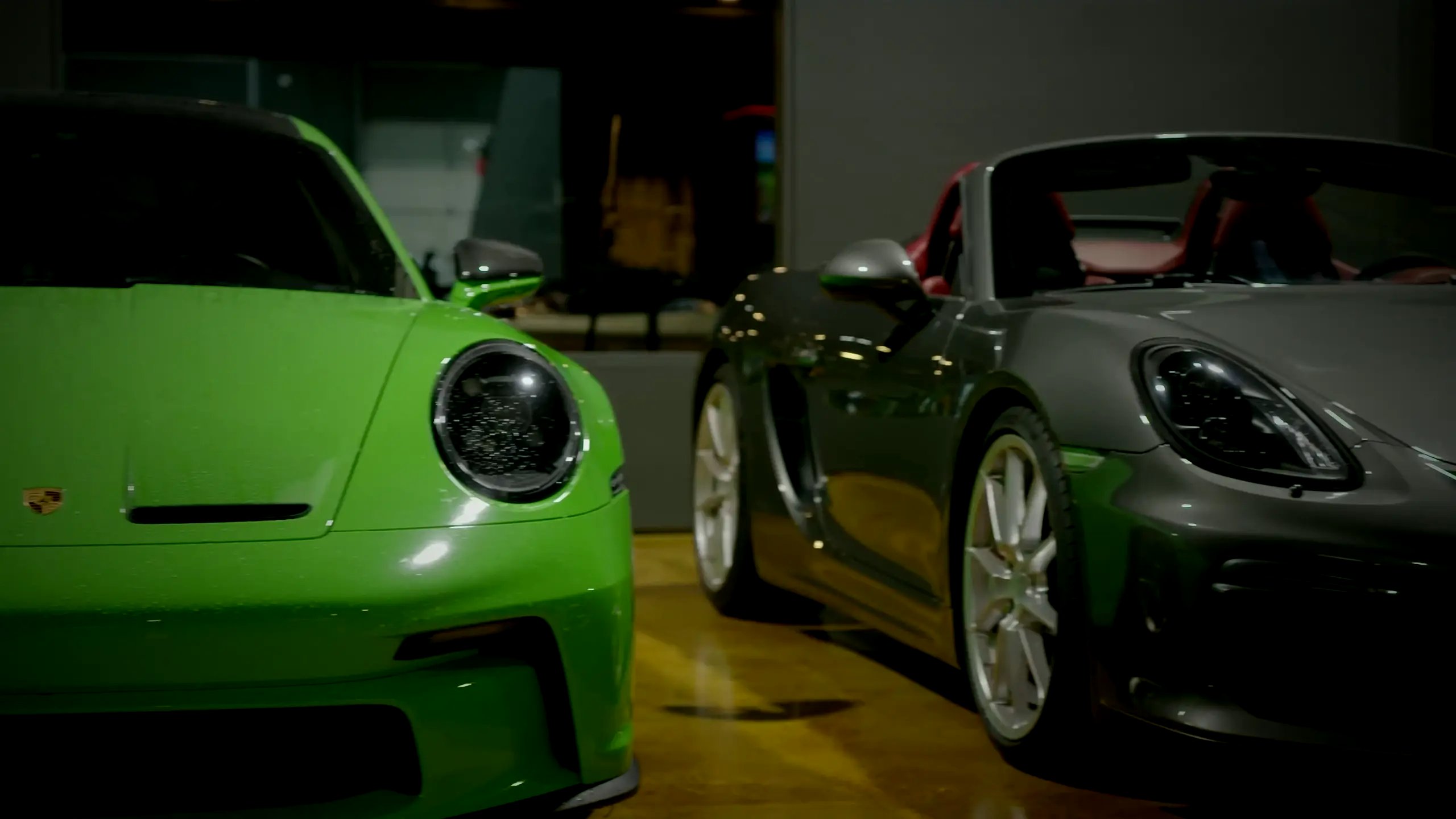 A green Porsche 911 GT3 and a grey Porsche Boxster Spyder on the floor at The Ride Lounge